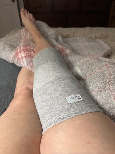 Reviewer wearing the grey Premium Bamboo Knee Sleeve on their leg while resting in bed.